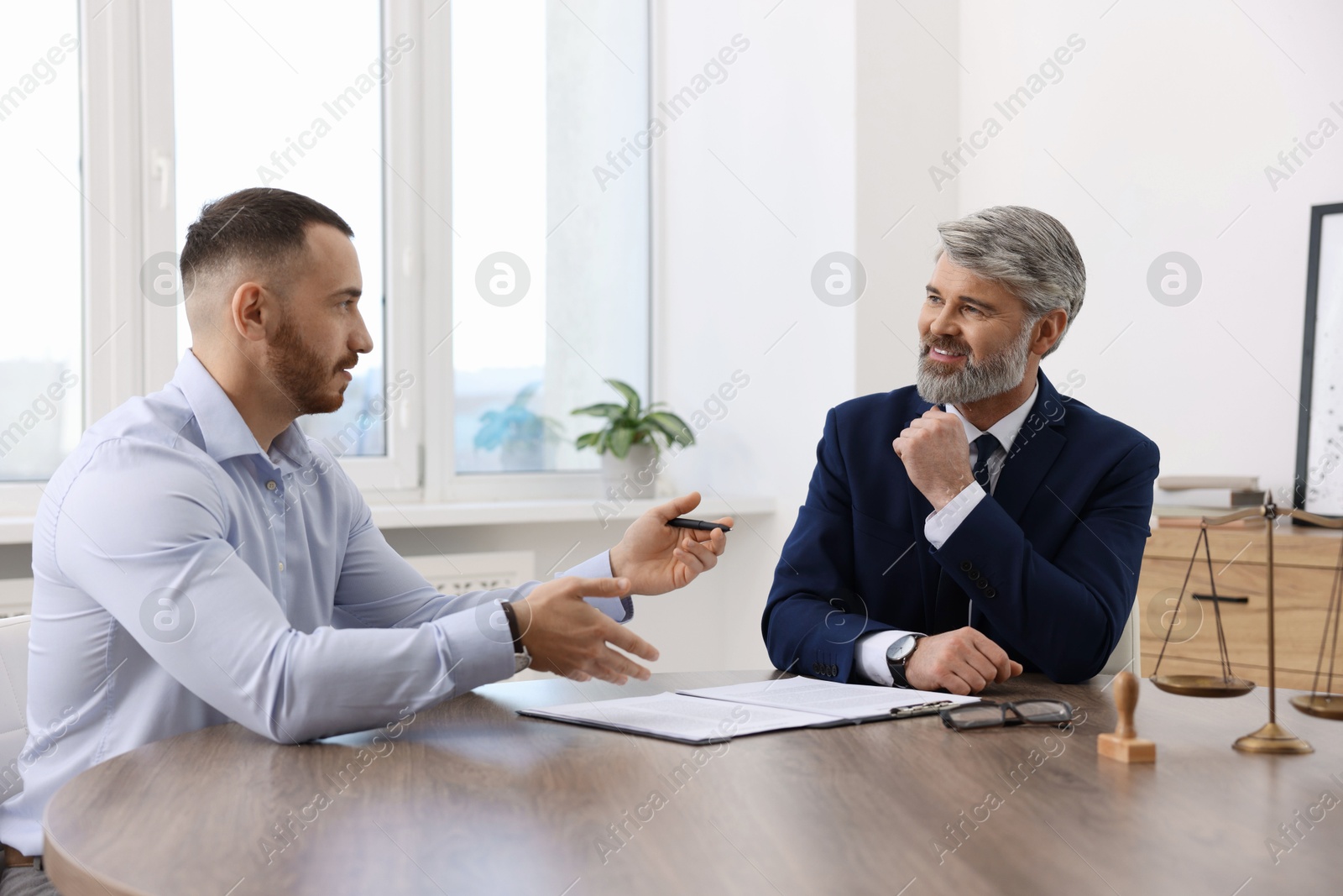 Photo of Man having meeting with professional lawyer at wooden desk indoors