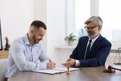 Client signing notarial paperwork during meeting with lawyer at wooden desk indoors