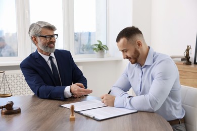 Client signing notarial paperwork during meeting with lawyer at wooden desk indoors