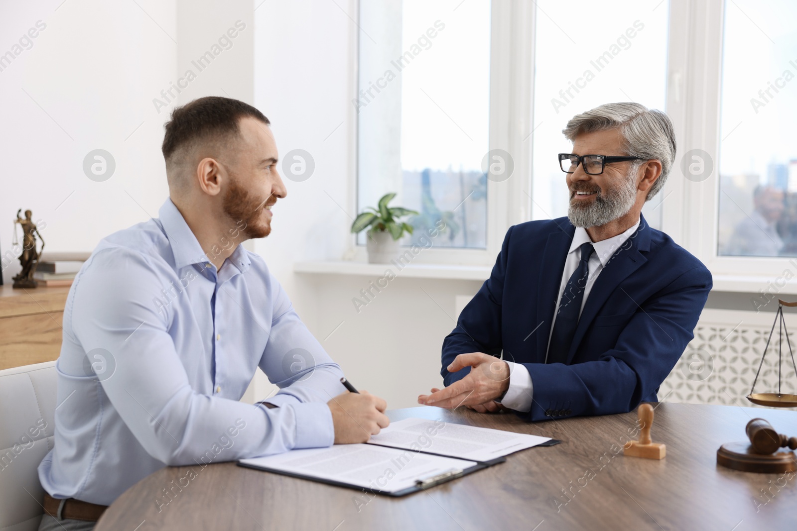 Photo of Client signing notarial paperwork during meeting with lawyer at wooden desk indoors