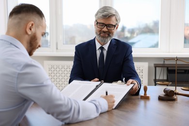 Client signing notarial paperwork during meeting with lawyer at wooden desk indoors