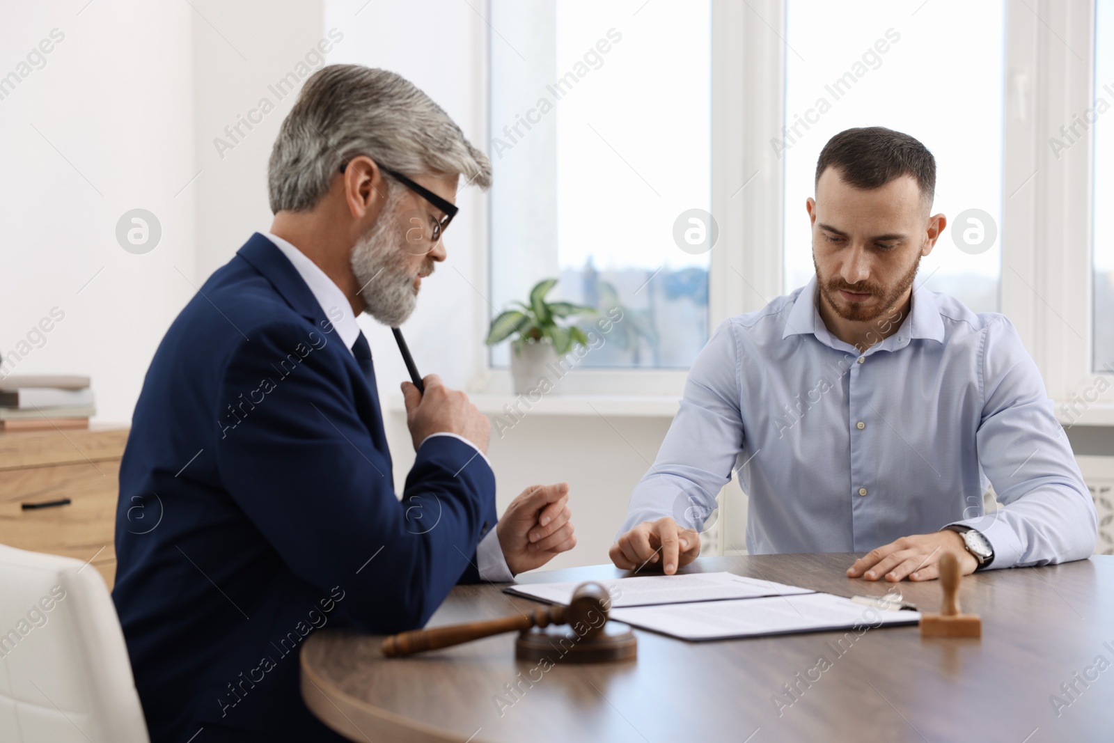 Photo of Man having meeting with professional lawyer at wooden desk indoors