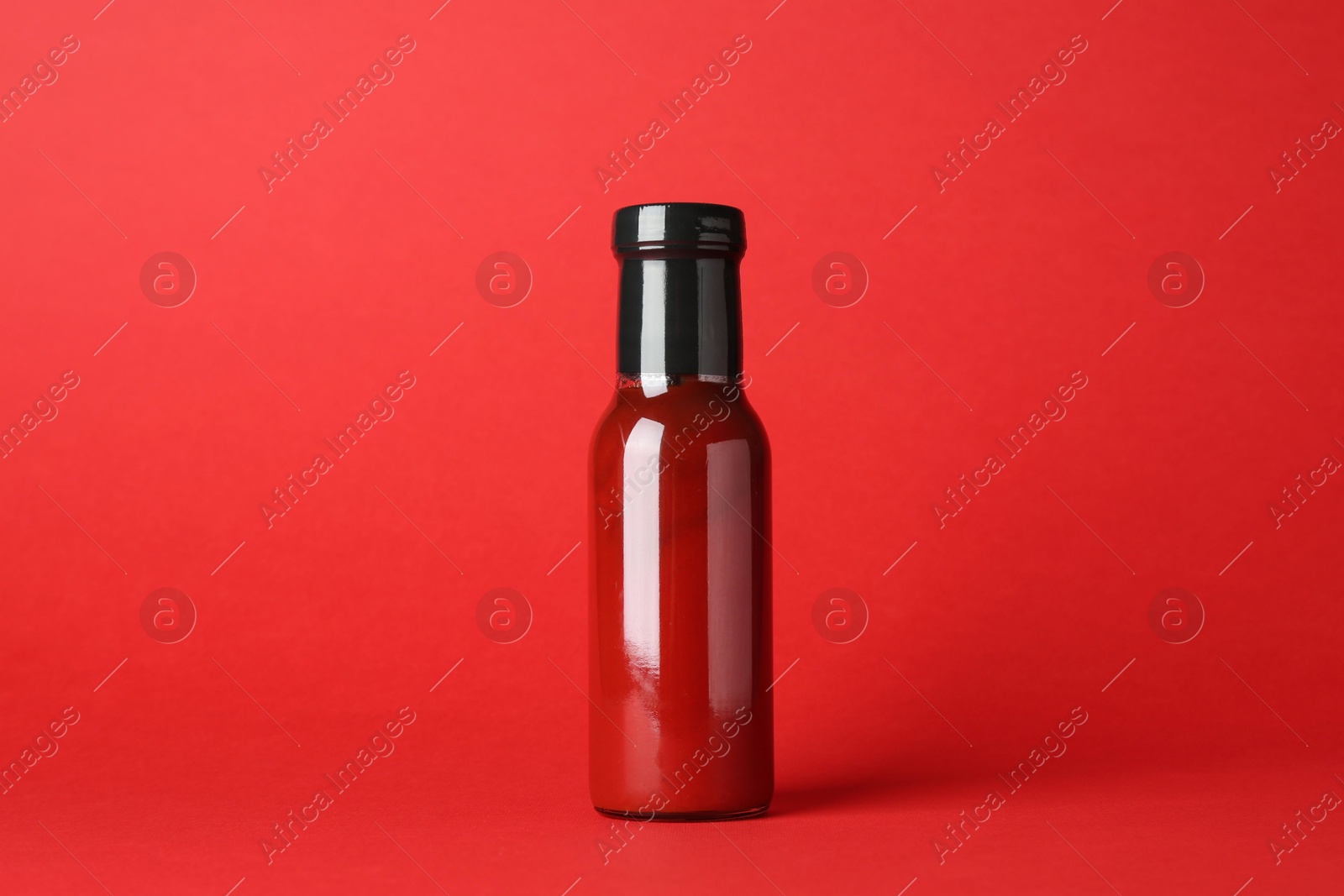 Photo of Ketchup in glass bottle on red background