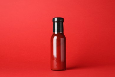 Photo of Ketchup in glass bottle on red background