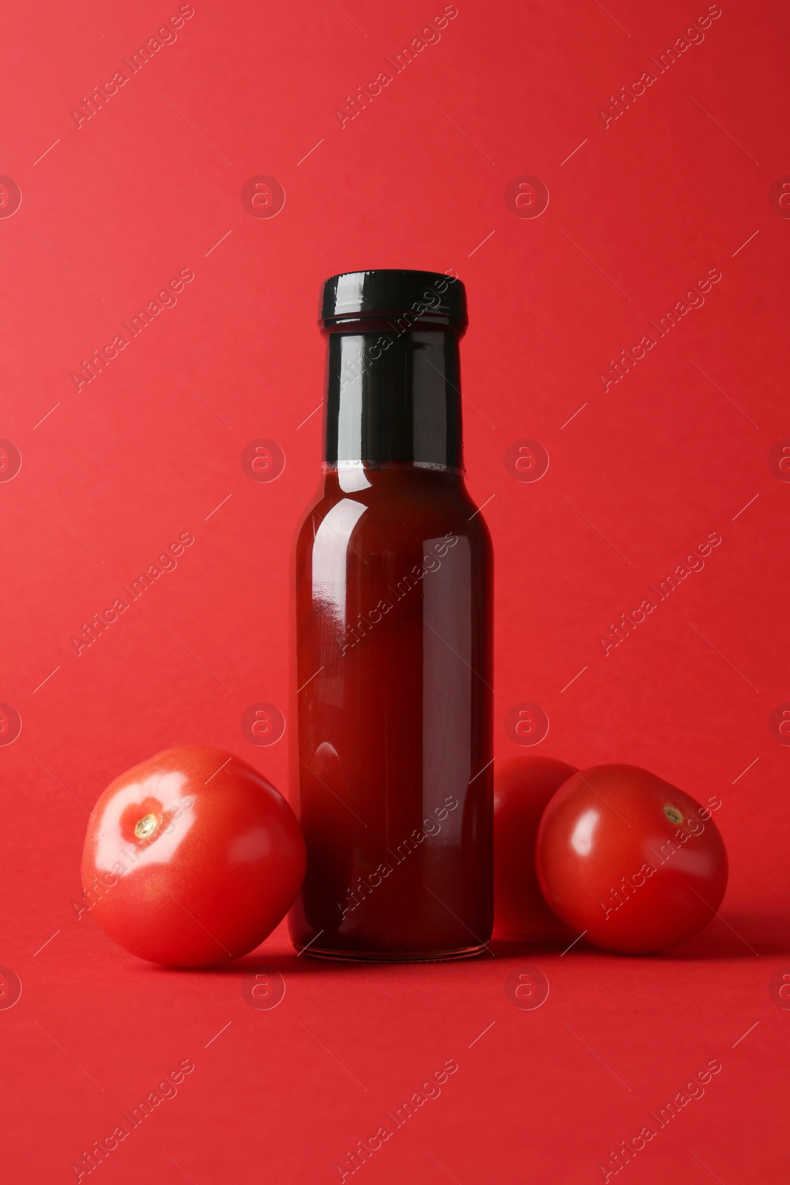 Photo of Ketchup in glass bottle and fresh tomatoes on red background