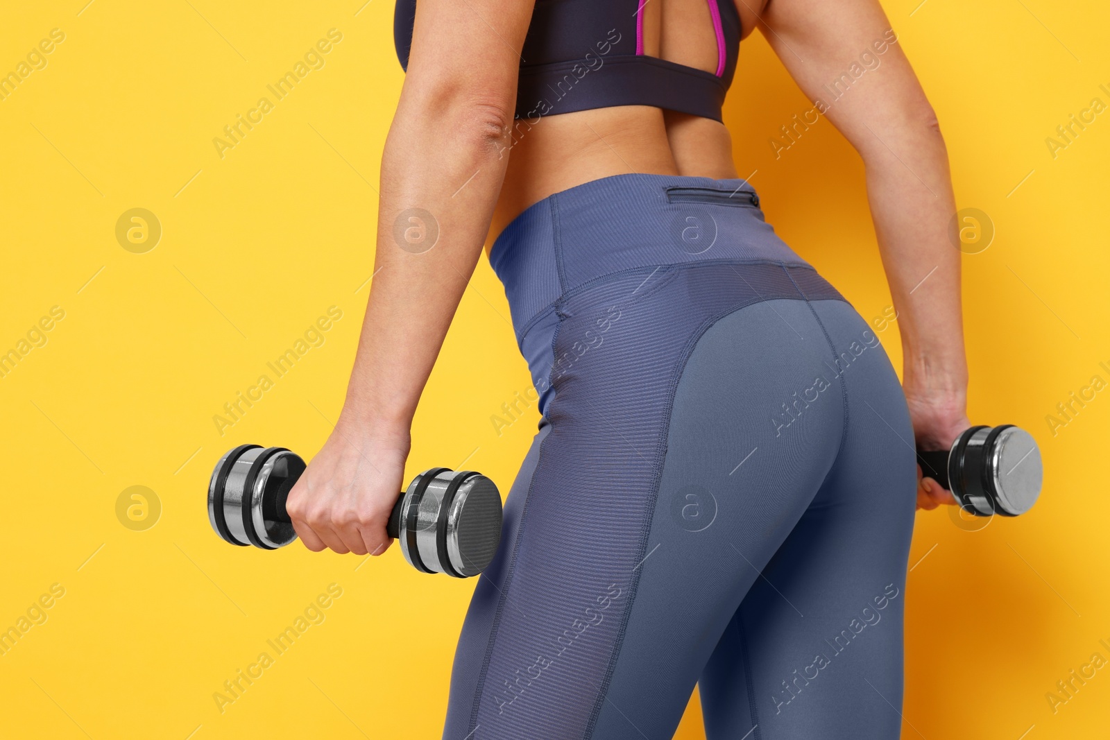 Photo of Woman with dumbbells training on yellow background, closeup