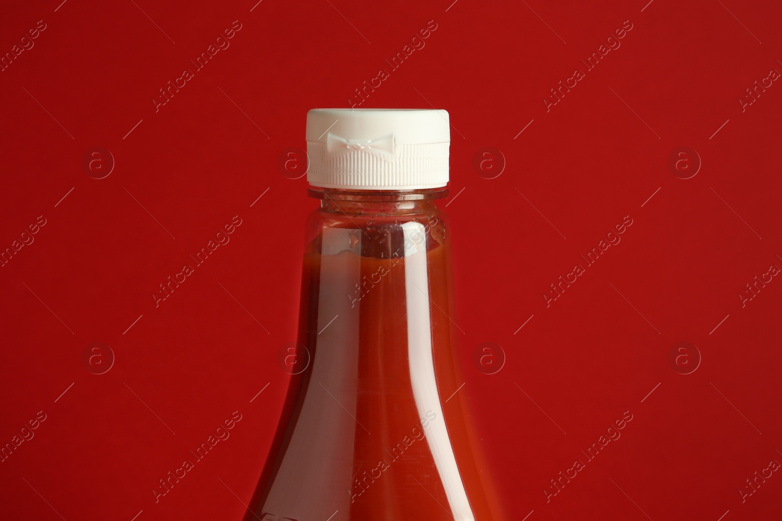 Photo of Tasty ketchup in bottle on red background, closeup