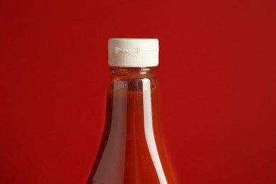 Photo of Tasty ketchup in bottle on red background, closeup