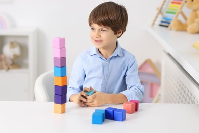 Photo of Happy boy with tower of colorful cubes at table indoors