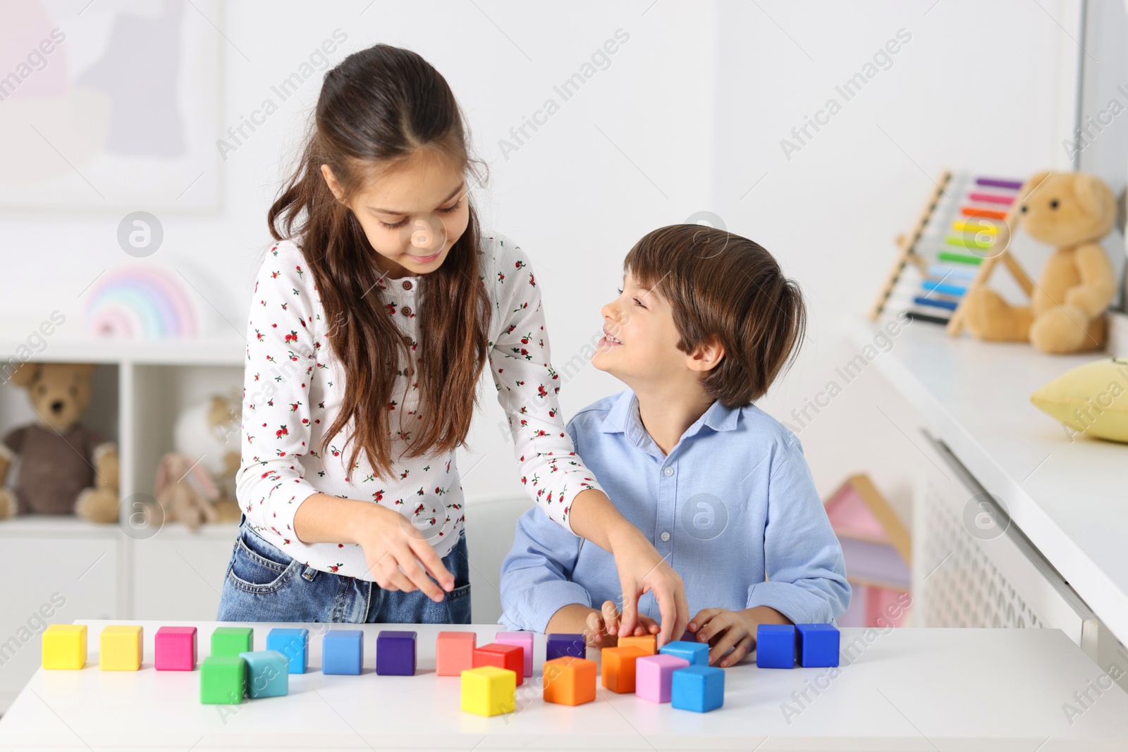 Photo of Children playing with colorful cubes at table indoors