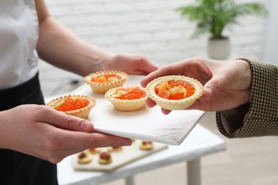 Photo of Woman taking tasty canape from waiter with board indoors, closeup