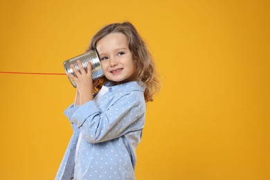 Girl using tin can telephone on orange background. Space for text