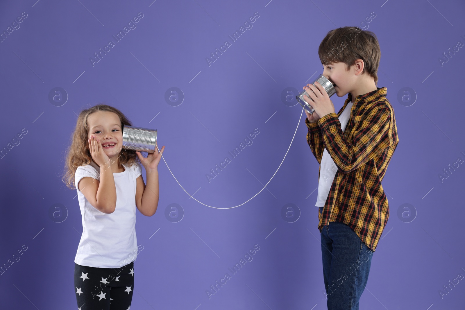 Photo of Boy and girl talking on tin can telephone against violet background