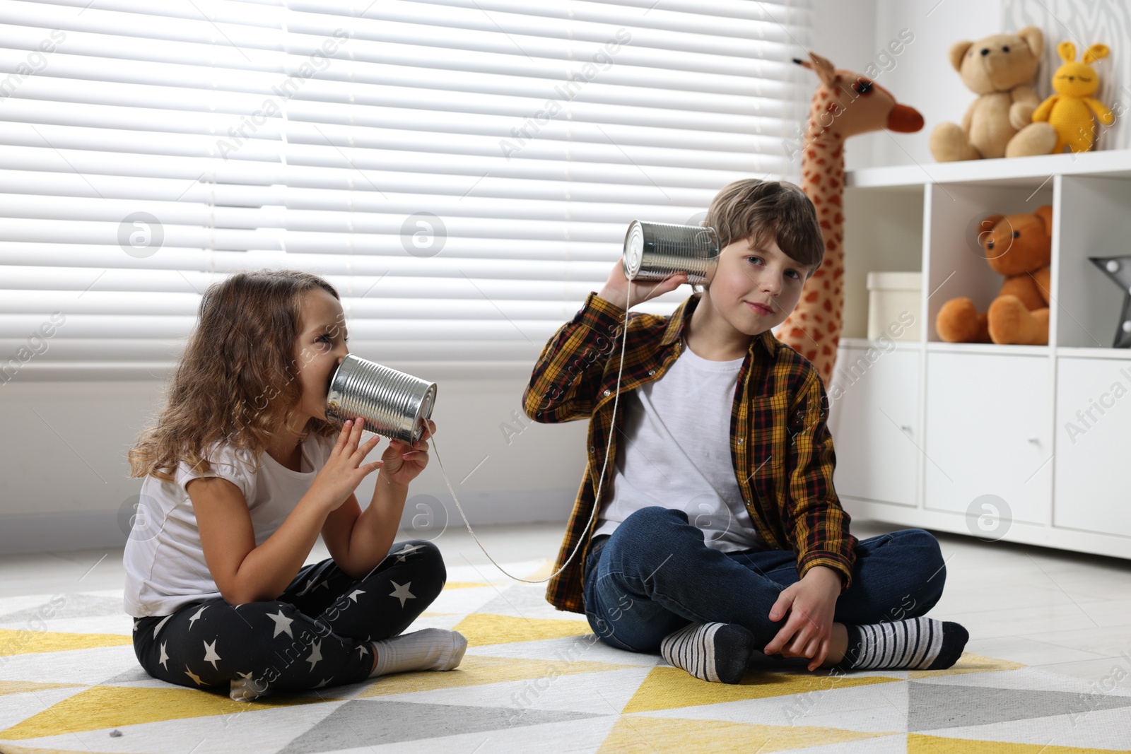 Photo of Boy and girl talking on tin can telephone indoors