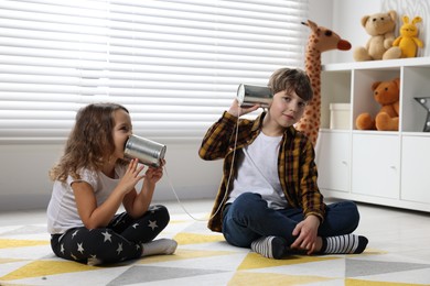 Photo of Boy and girl talking on tin can telephone indoors