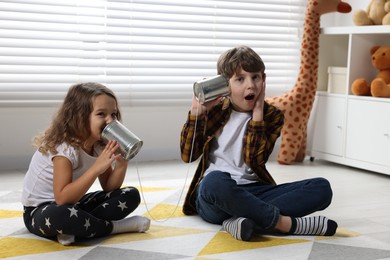 Photo of Boy and girl talking on tin can telephone indoors