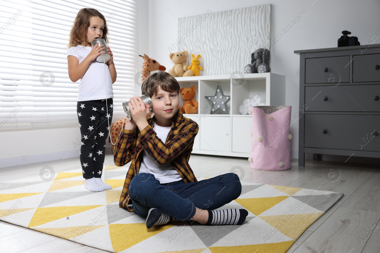 Photo of Boy and girl talking on tin can telephone indoors