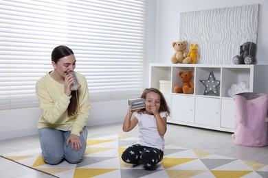 Photo of Woman and girl talking on tin can telephone indoors