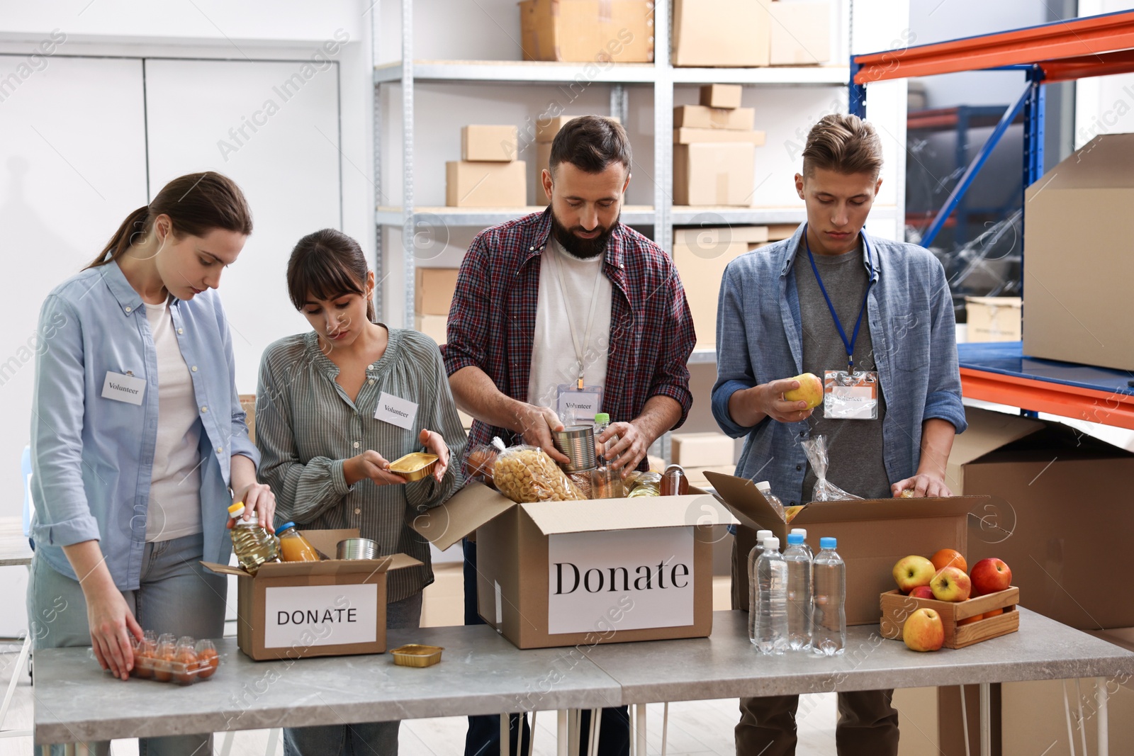 Photo of Group of volunteers packing food donations at table indoors