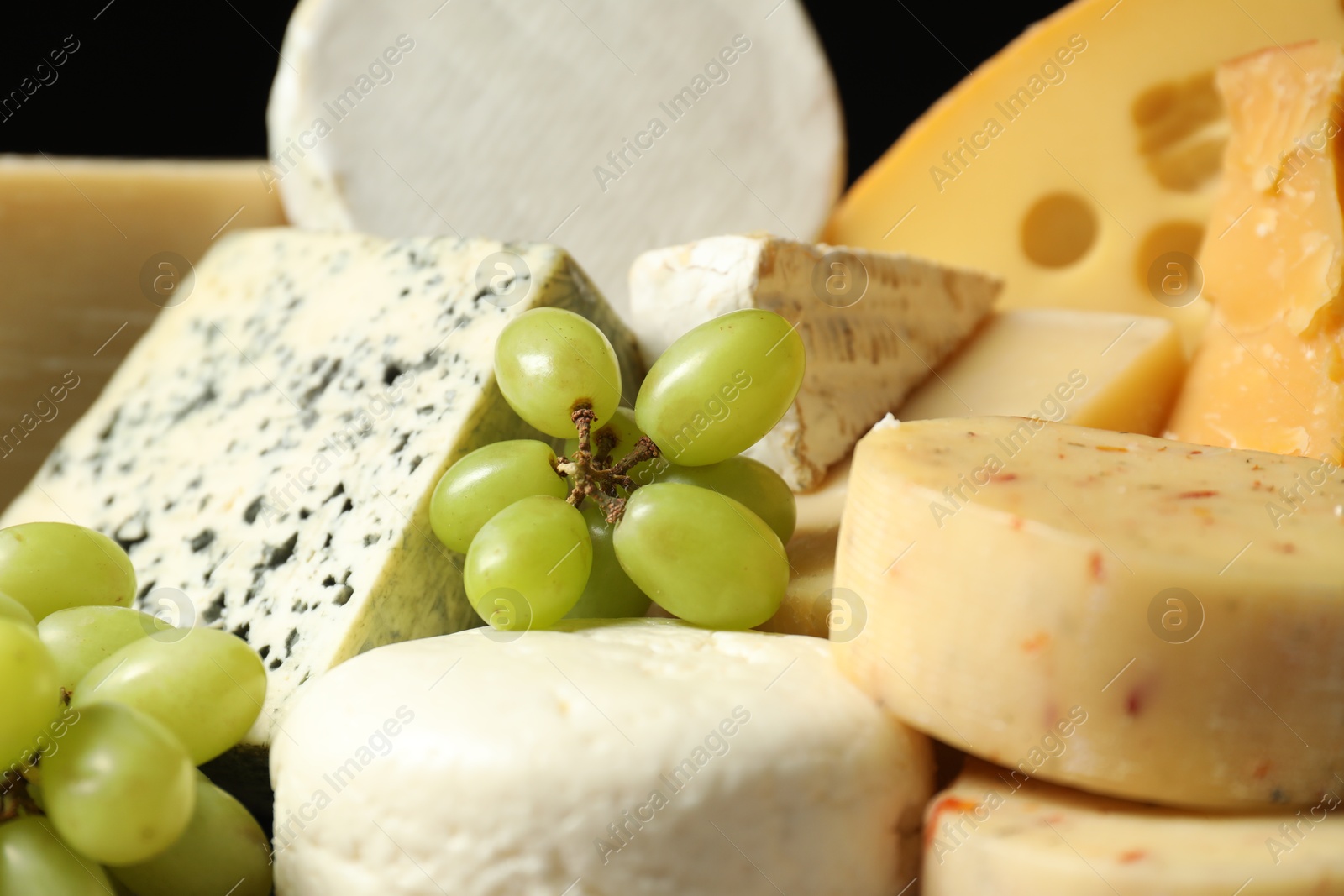 Photo of Different types of cheese and grapes on black background, closeup