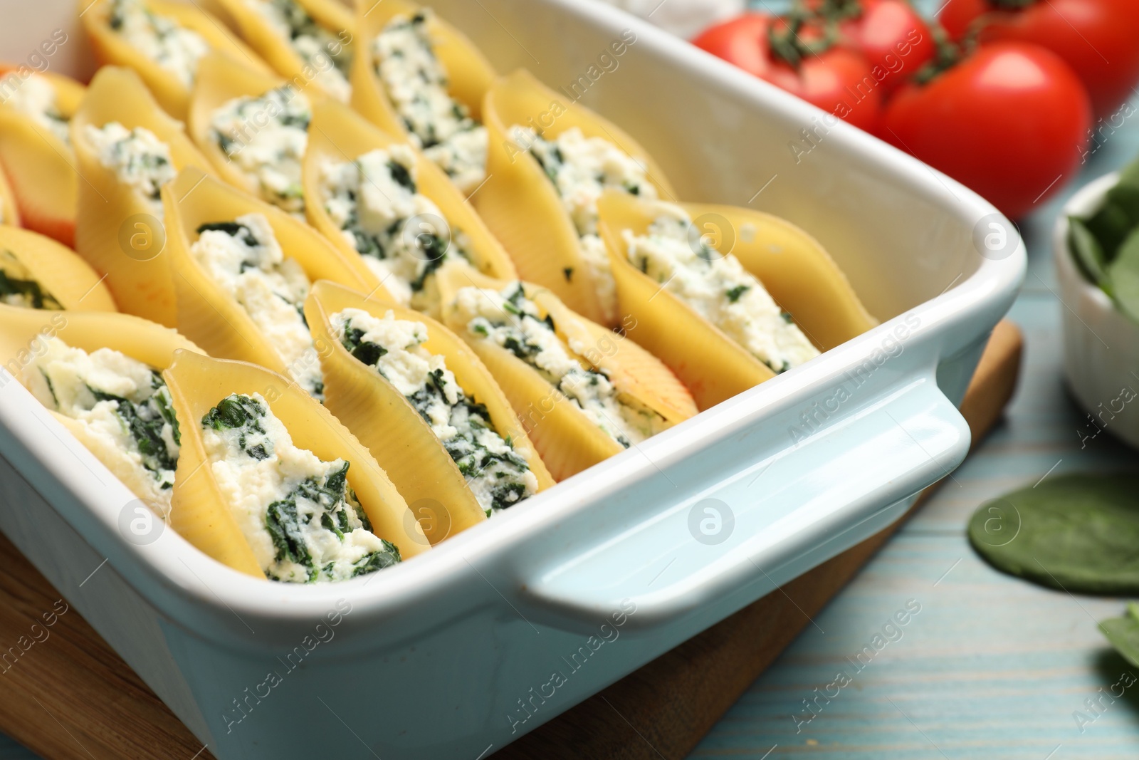 Photo of Delicious conchiglie pasta with ricotta cheese and spinach in baking dish on light blue wooden table, closeup