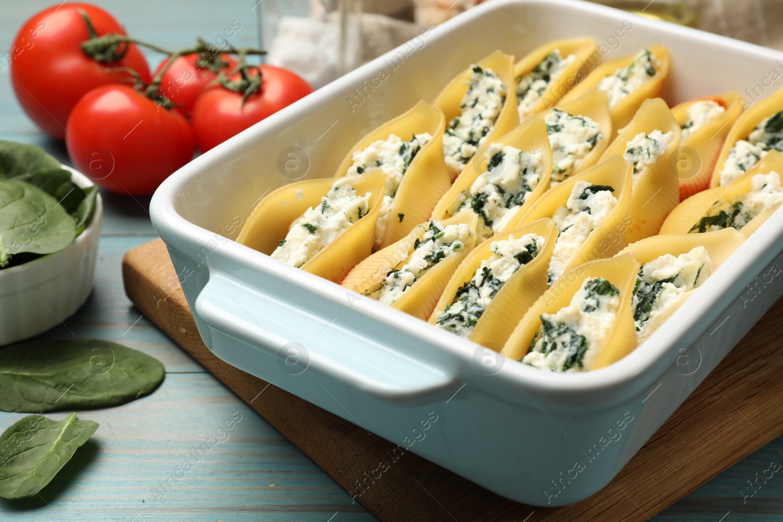 Photo of Delicious conchiglie pasta with ricotta cheese and spinach in baking dish on light blue wooden table, closeup