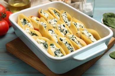 Photo of Delicious conchiglie pasta with ricotta cheese and spinach in baking dish on light blue wooden table, closeup