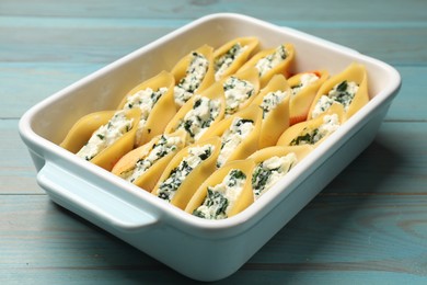 Photo of Delicious pasta with ricotta cheese and spinach in baking dish on light blue wooden table, closeup