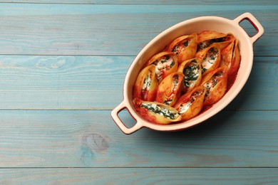 Photo of Delicious pasta with ricotta cheese, spinach and tomato sauce in baking dish on light blue wooden table, top view. Space for text