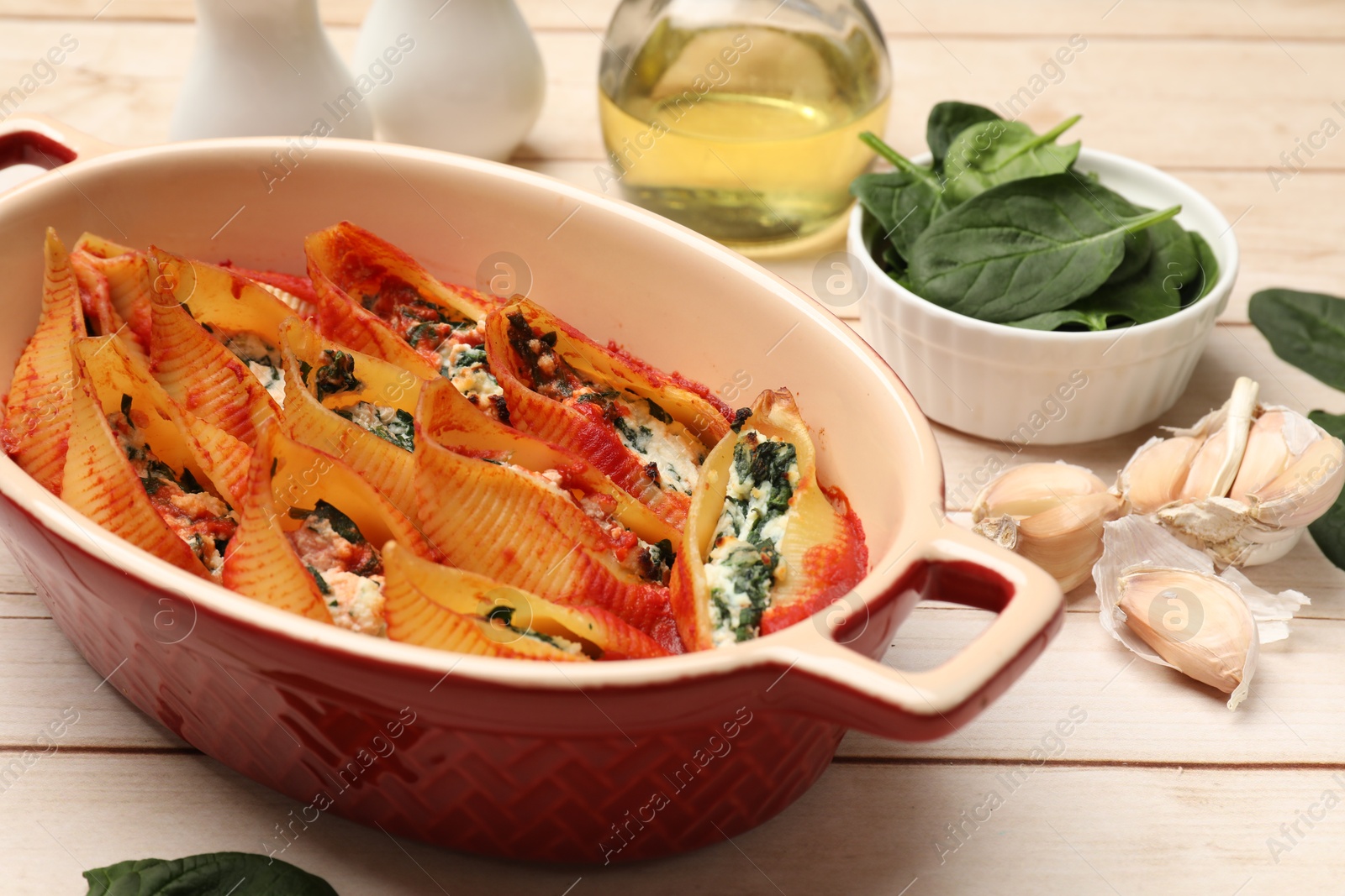 Photo of Delicious pasta with ricotta cheese, spinach and tomato sauce in baking dish on wooden table, closeup