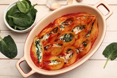 Photo of Delicious pasta with ricotta cheese, spinach and tomato sauce in baking dish on wooden table, flat lay