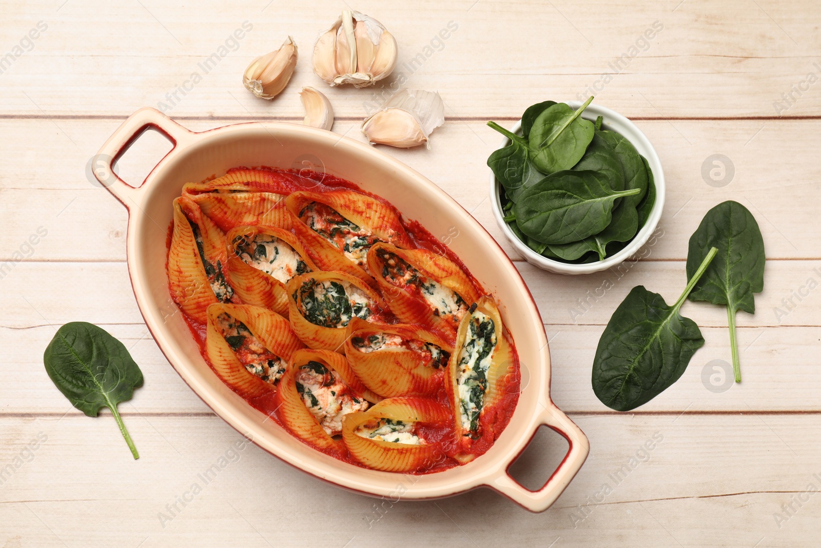 Photo of Delicious pasta with ricotta cheese, spinach and tomato sauce in baking dish on wooden table, flat lay