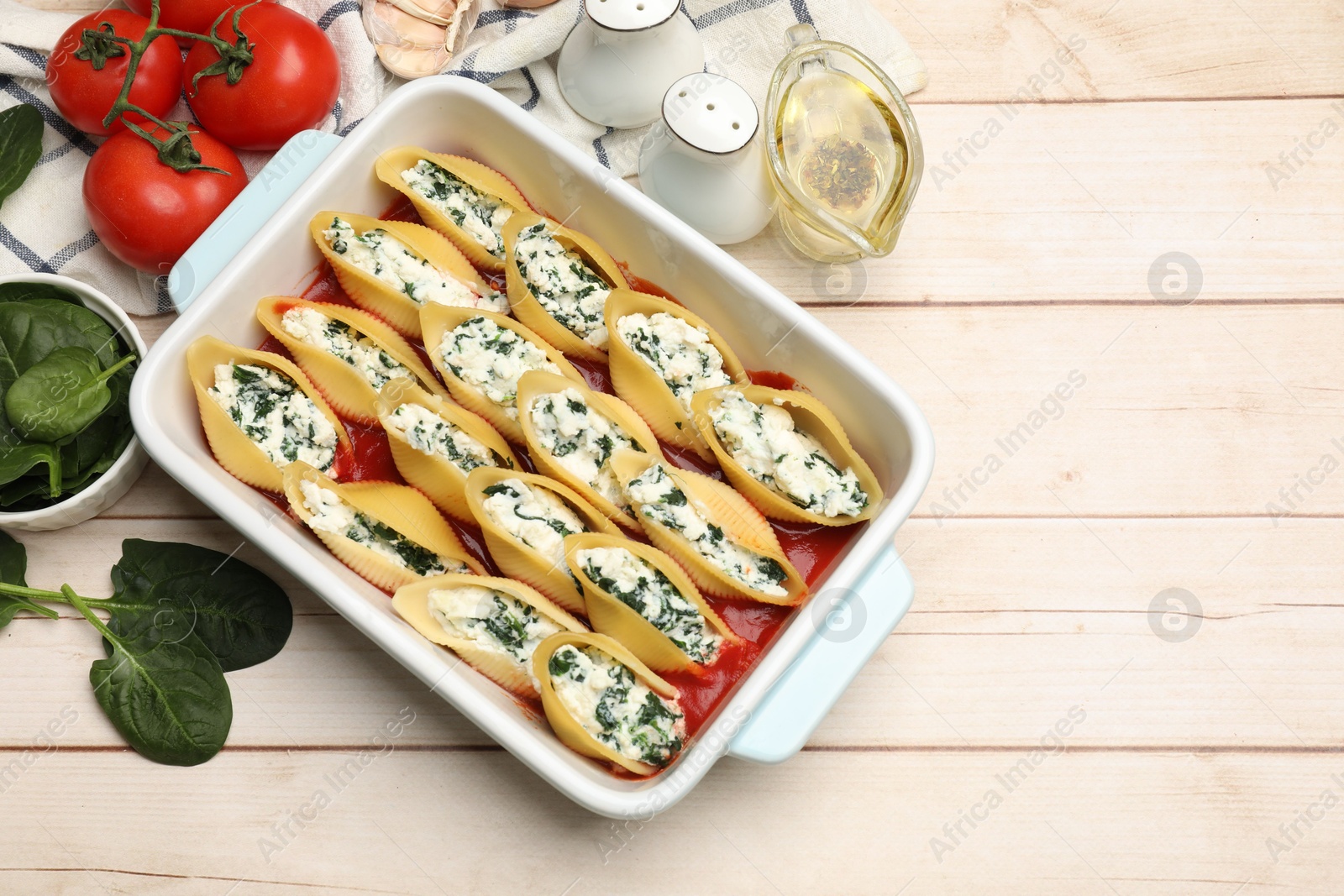 Photo of Delicious pasta with ricotta cheese, spinach and tomato sauce in baking dish on wooden table, flat lay. Space for text