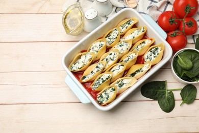 Photo of Delicious pasta with ricotta cheese, spinach and tomato sauce in baking dish on wooden table, flat lay. Space for text