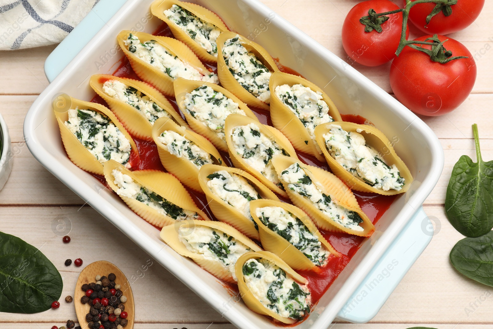 Photo of Delicious pasta with ricotta cheese, spinach and tomato sauce in baking dish on wooden table, flat lay