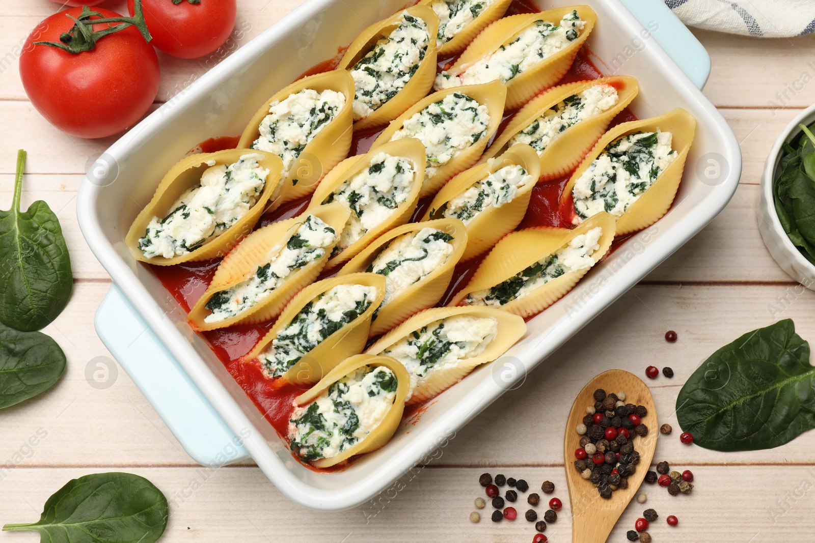 Photo of Delicious pasta with ricotta cheese, spinach and tomato sauce in baking dish on wooden table, flat lay