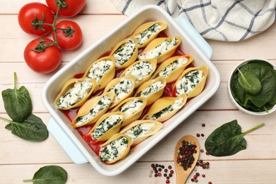 Photo of Delicious pasta with ricotta cheese, spinach and tomato sauce in baking dish on wooden table, flat lay