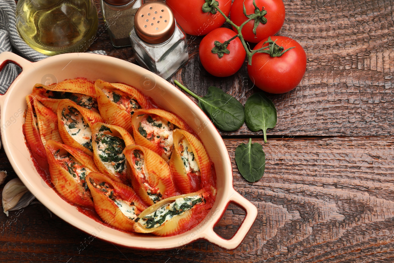 Photo of Delicious conchiglie pasta with ricotta cheese, spinach and tomato sauce in baking dish on wooden table, flat lay. Space for text