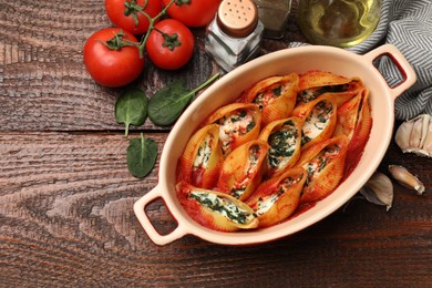 Photo of Delicious conchiglie pasta with ricotta cheese, spinach and tomato sauce in baking dish on wooden table, flat lay. Space for text