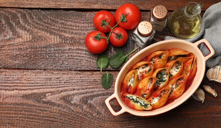 Photo of Delicious conchiglie pasta with ricotta cheese, spinach and tomato sauce in baking dish on wooden table, flat lay. Space for text