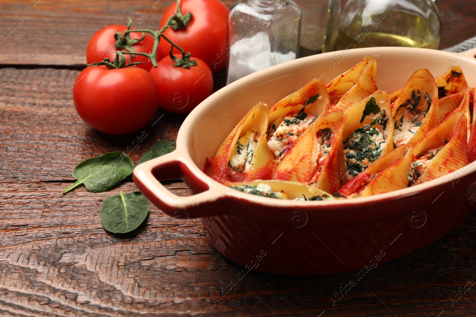 Photo of Delicious pasta with ricotta cheese, spinach and tomato sauce in baking dish on wooden table, closeup