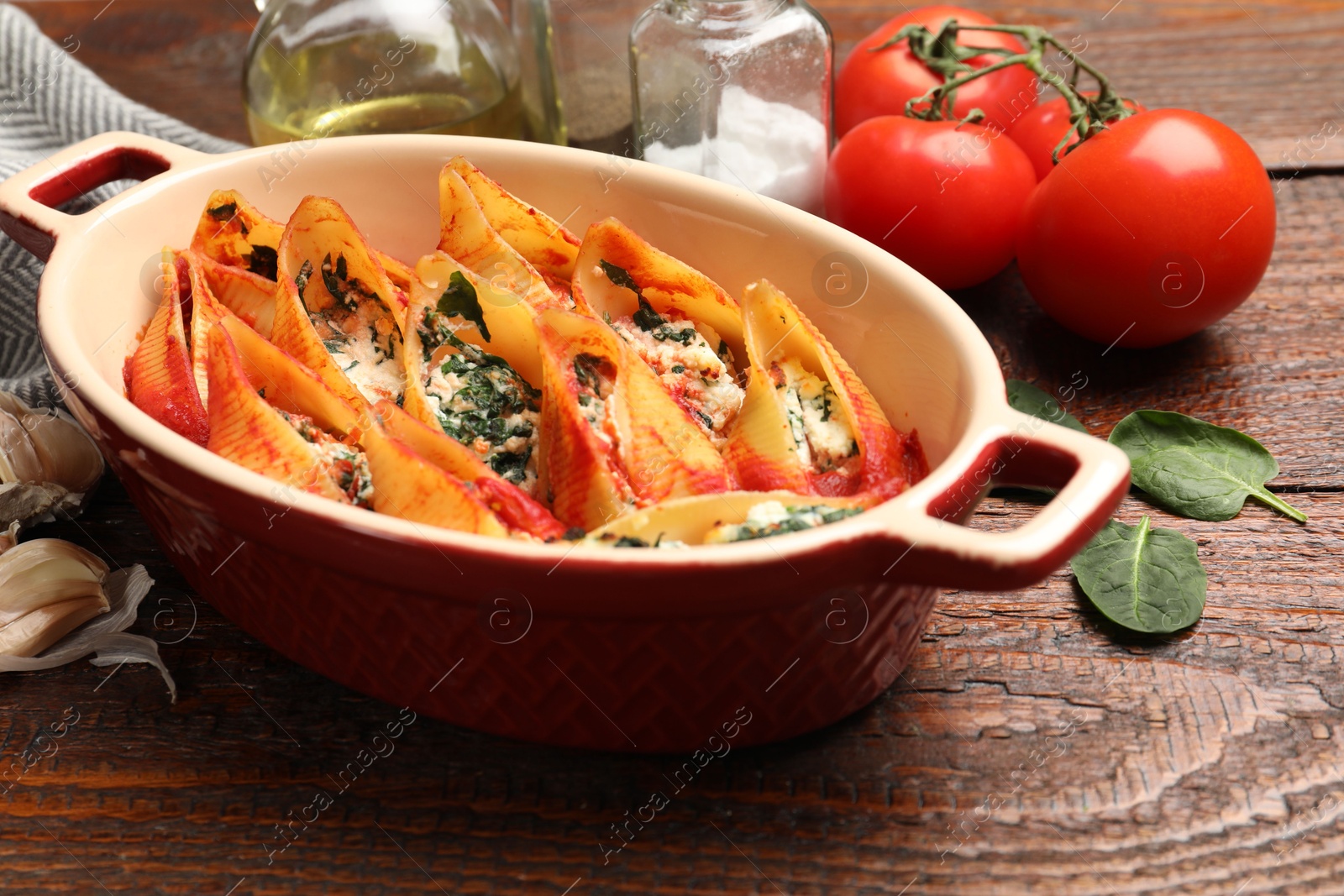 Photo of Delicious pasta with ricotta cheese, spinach and tomato sauce in baking dish on wooden table, closeup