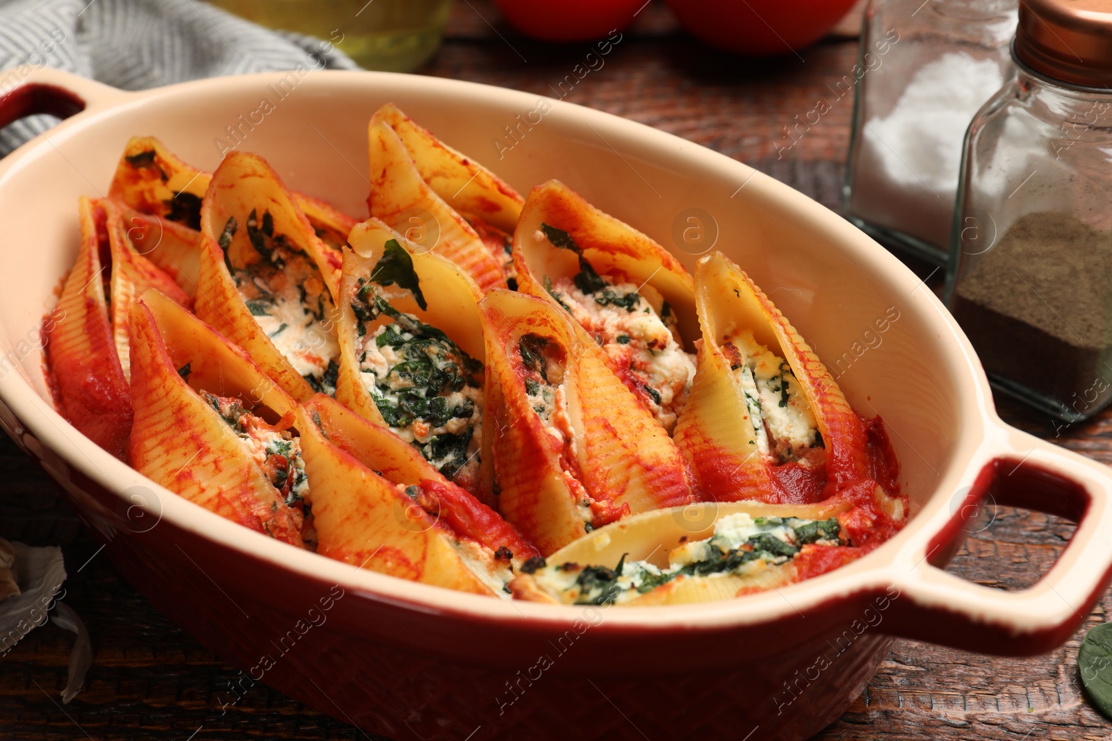 Photo of Delicious conchiglie pasta with ricotta cheese, spinach and tomato sauce in baking dish on wooden table, closeup