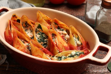 Photo of Delicious conchiglie pasta with ricotta cheese, spinach and tomato sauce in baking dish on wooden table, closeup