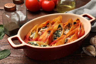 Photo of Delicious conchiglie pasta with ricotta cheese, spinach and tomato sauce in baking dish on wooden table, closeup