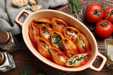 Photo of Delicious conchiglie pasta with ricotta cheese, spinach and tomato sauce in baking dish on wooden table, flat lay