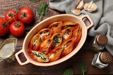 Photo of Delicious conchiglie pasta with ricotta cheese, spinach and tomato sauce in baking dish on wooden table, flat lay