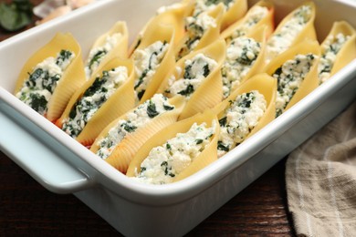 Photo of Delicious conchiglie pasta with ricotta cheese and spinach in baking dish on wooden table, closeup