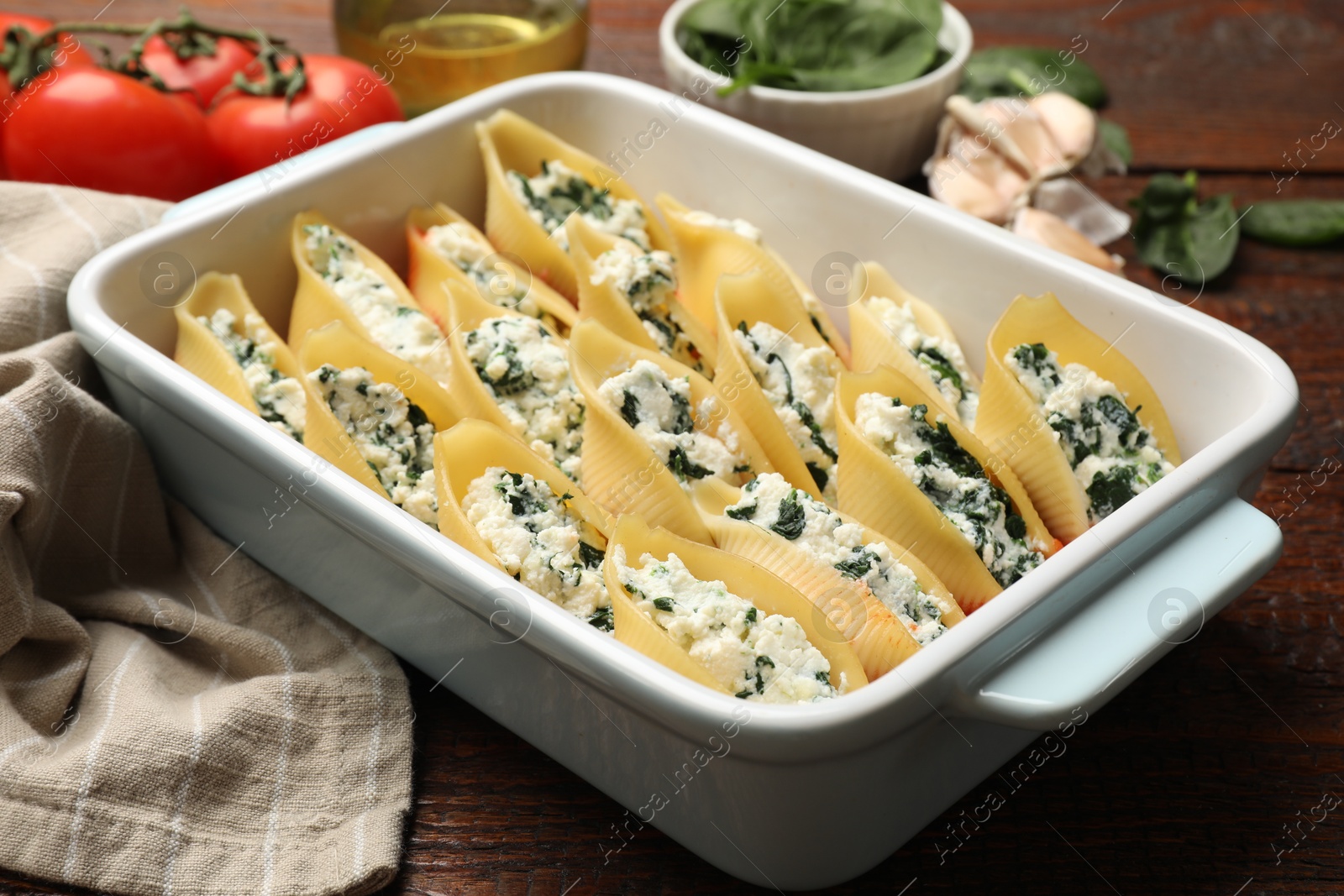 Photo of Delicious conchiglie pasta with ricotta cheese and spinach in baking dish on wooden table, closeup