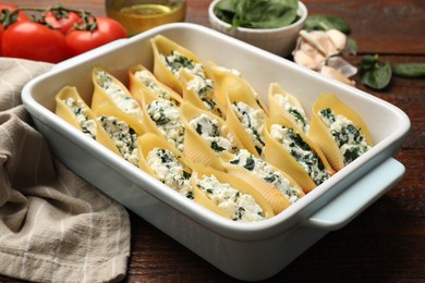 Photo of Delicious conchiglie pasta with ricotta cheese and spinach in baking dish on wooden table, closeup